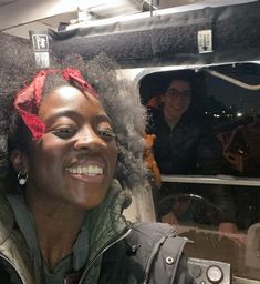 a woman with an afro is smiling in the back of a bus as people look on