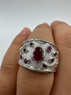 a woman's hand holding a silver ring with red stones