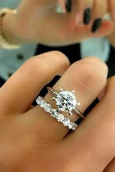 a woman's hand with two engagement rings on her finger and the ring is in front of her face