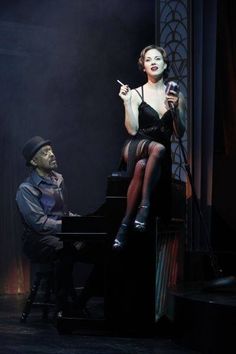 a woman sitting on top of a piano next to a man holding a cell phone