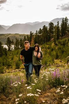 a man and woman walking through a field with wildflowers in the foreground