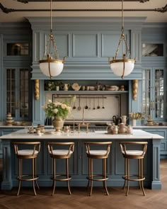 a large kitchen with blue cabinets and marble counter tops, along with four stools in front of the island