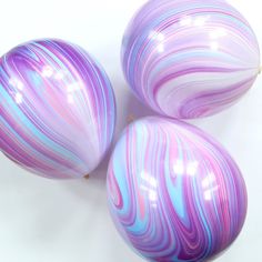 three purple and blue marbled balls sitting on top of a white countertop next to each other