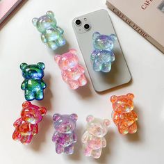 there are many different colored bears on the table next to a cell phone and camera