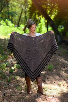 a woman is standing in the woods holding a shawl over her head and wearing boots