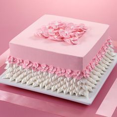 a pink and white square cake with flowers on the top is sitting on a table