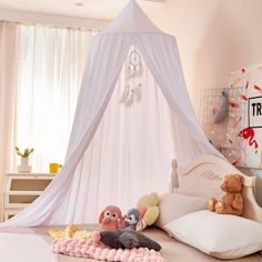 a white canopy bed with stuffed animals on the bottom and pillows underneath it in a girls'bedroom