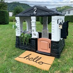 a fake hello kitty house in the grass with a welcome mat on the ground next to it