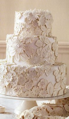 a three tiered white wedding cake with flowers on top and lace around the edges