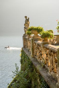 a boat is in the water near a stone wall with statues on it and some plants