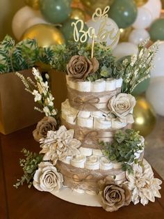 a three tiered cake decorated with flowers and greenery sits on a table in front of balloons