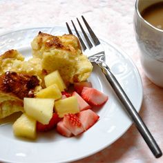 a white plate topped with fruit next to a fork and cup of coffee on top of a table