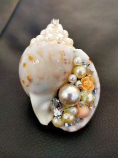 a seashell with pearls and other jewels on it's side sitting on a black surface