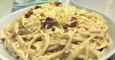 a white bowl filled with pasta and meat covered in cheese sauce on top of a colorful table cloth