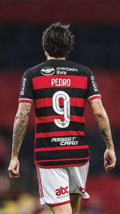 a soccer player with tattoos on his arms and legs, wearing a black and red uniform