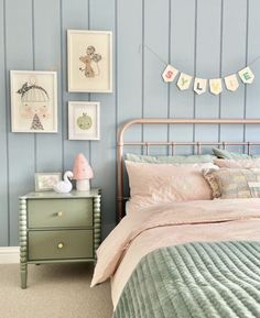 a bedroom with blue walls, pink bedding and pictures on the wall above it