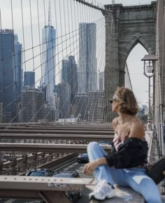 a woman sitting on a bench in front of the brooklyn bridge looking out over the city