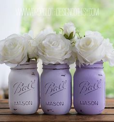 three painted mason jars with white roses in them