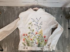 a white jacket with flowers painted on the front and back, sitting on top of a wooden floor