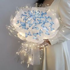 a woman is holding a bouquet with blue butterflies on it and lights in the center