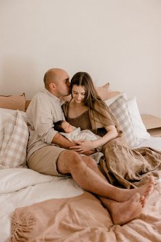 a man and woman cuddle on top of a bed while holding a baby in their arms