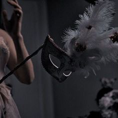 a woman wearing a mask with feathers flying around her face and holding a stick in front of her face