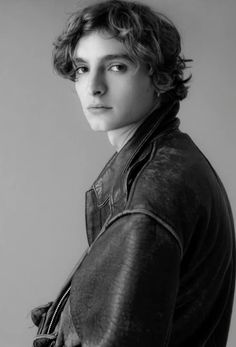 a black and white photo of a young man with curly hair wearing a leather jacket