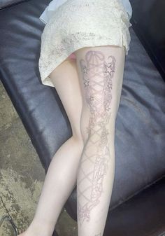 a woman sitting on top of a black couch next to her legs covered in tattoos