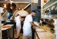 two men working in a restaurant kitchen preparing pizzas on the counter and cooking them