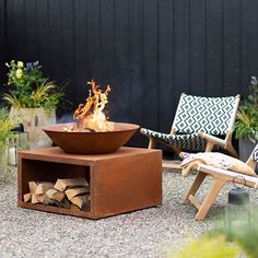 a fire pit sitting in the middle of a gravel area next to two lawn chairs