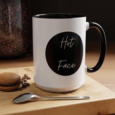 a white and black coffee mug with the words hot face on it next to a spoon