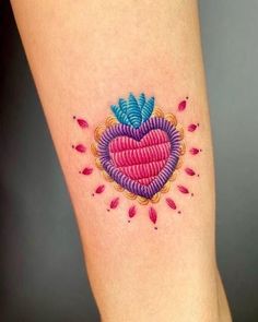 a heart shaped tattoo on the leg with pink and blue flowers around it's edges