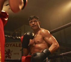 a shirtless man in boxing gloves standing next to a punching glove on the ground