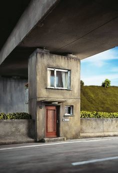 a small building with a red door and window on the side of a road under a bridge