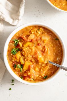 two bowls filled with soup on top of a white table next to a napkin and spoon