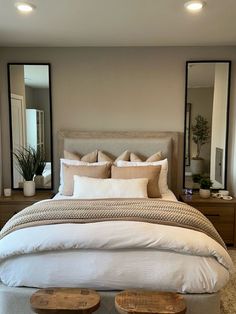 a large bed sitting in a bedroom next to two mirrors and a footstool