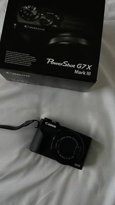 a black camera sitting on top of a white bed next to a box that says powershot g7x