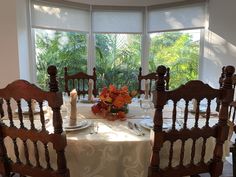 a dining room table set for four with flowers in the center and candles on top