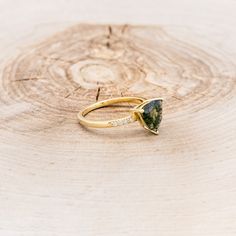 a gold ring with a green tourmaline stone in the center on top of a tree stump