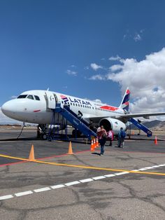 an airplane is parked on the tarmac with people walking up to it and another plane in the background