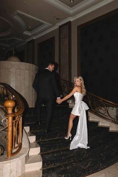 a man and woman in formal wear walking down the stairs at their wedding reception, holding hands