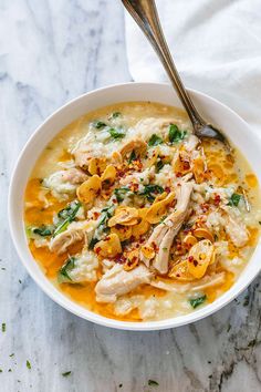 a bowl of chicken and rice soup with a spoon in it on a marble surface