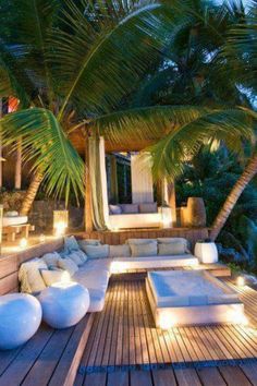 an outdoor lounge area with palm trees and lights on the deck, overlooking the ocean