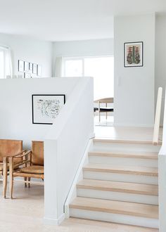 a white staircase with wooden chairs and pictures on the wall