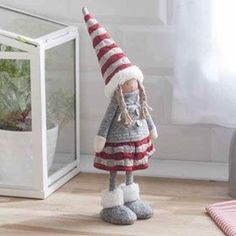 a knitted gnome doll standing in front of a glass case with plants inside it