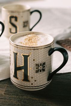 two coffee mugs sitting on top of a table next to each other with the letter h painted on them