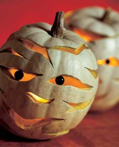 two carved pumpkins sitting on top of a wooden table with eyes painted on them