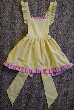 This Fluttershy inspired pinafore style apron features a machine embroidered cutie mark and ruffled contrasting trim.  The adjustable shoulder straps can cross in the back and button along the waistband or they can be tied behind the neck.  Tied fully closed, this apron fits a child's size SM.  It is great for Halloween or just to play dress up. Made of cotton.  Wash cold, hang dry, and iron on medium heat. AVAILABLE IN OTHER COLORS.  IF YOU ARE LOOKING FOR A SPECIFIC PONY, PLEASE MESSAGE ME. CUSTOM SIZE AVAILABLE UPON REQUEST. ALSO AVAILABLE IN ADULT'S SIZE!! Trans Masc Fluttershy, Fluttershy Clothes, Fluttercord Child, Fluttershy Collection, Fluttershy Mlp, Apron Yellow, Play Dress Up, Pinafore Apron, Girls Costumes