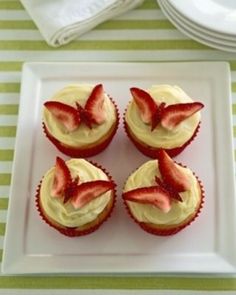 four cupcakes with strawberries on top are sitting on a square white plate