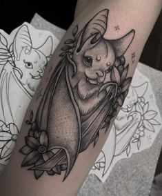 a black and white tattoo of a bat with flowers on its arm, in the shape of a flower